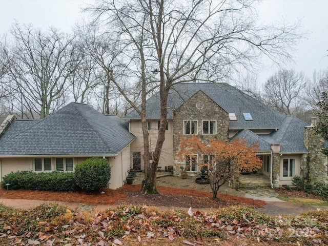 traditional home with stone siding, roof with shingles, a chimney, and stucco siding