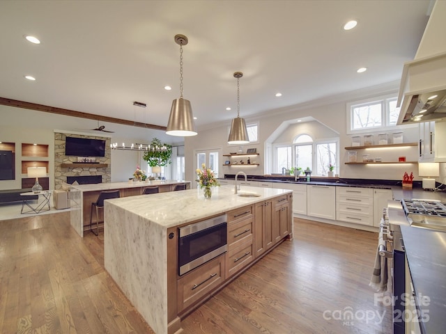 kitchen featuring a large island, open shelves, stainless steel microwave, dark stone countertops, and decorative light fixtures