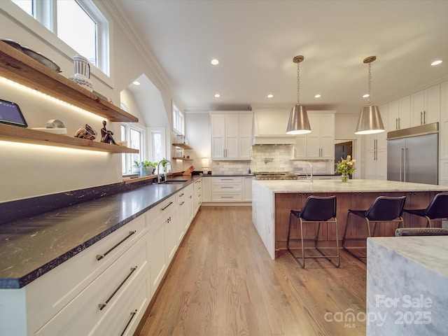 kitchen featuring built in fridge, decorative light fixtures, open shelves, white cabinetry, and a sink