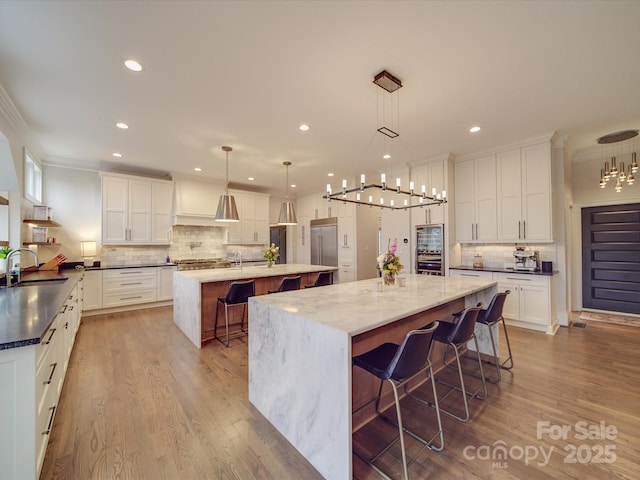 kitchen featuring pendant lighting, a breakfast bar area, white cabinetry, a sink, and a large island with sink