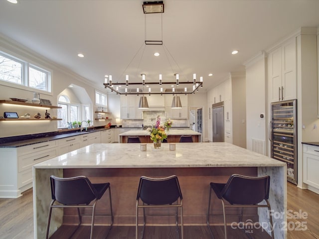 kitchen with beverage cooler, white cabinetry, a large island, dark stone countertops, and a kitchen bar