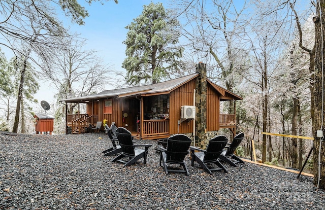 rear view of house featuring a deck, an outdoor fire pit, stone siding, board and batten siding, and a chimney