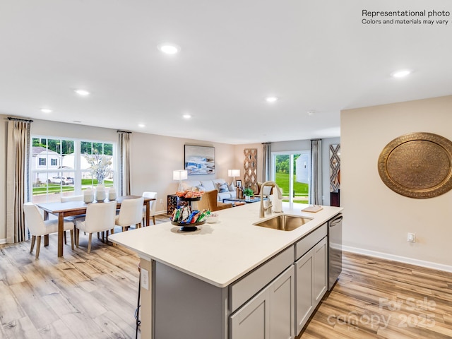 kitchen with gray cabinets, sink, light hardwood / wood-style floors, and a center island with sink