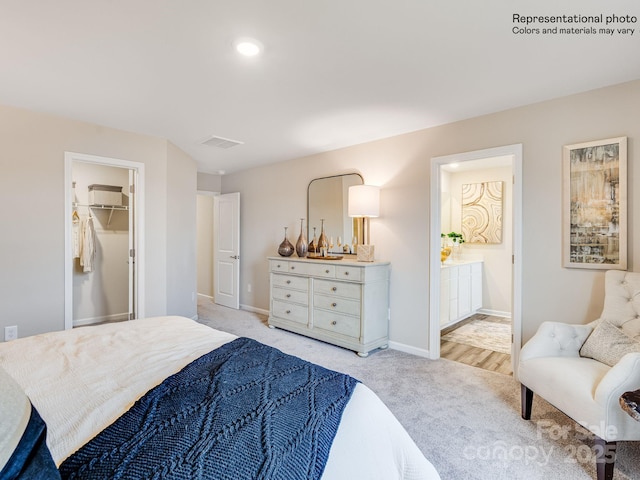 bedroom with ensuite bath, a spacious closet, and light colored carpet