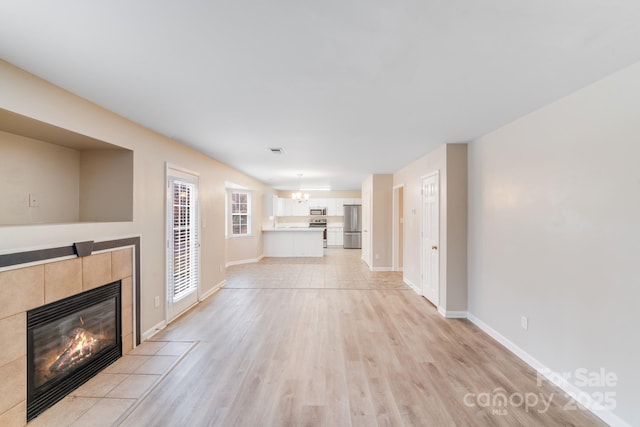 unfurnished living room with a chandelier, a fireplace, visible vents, baseboards, and light wood finished floors