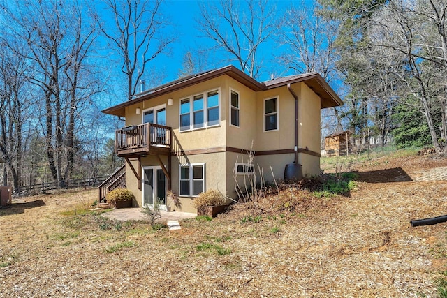 rear view of house with stucco siding, a patio, stairway, and fence