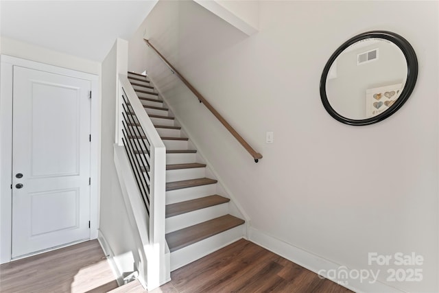 staircase with baseboards, visible vents, and wood finished floors