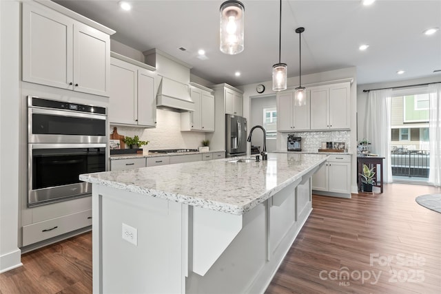 kitchen featuring a kitchen island with sink, appliances with stainless steel finishes, white cabinetry, and decorative light fixtures