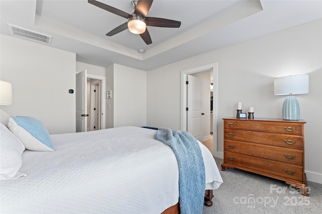 bedroom with a raised ceiling, light colored carpet, visible vents, a ceiling fan, and baseboards