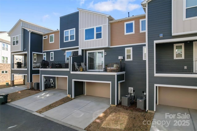 back of property with board and batten siding, cooling unit, driveway, and a garage