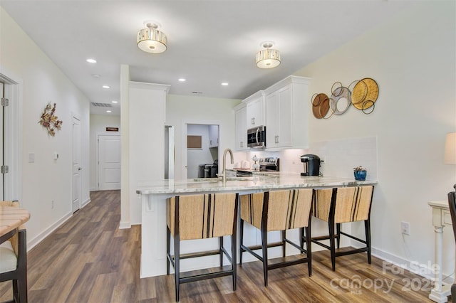 kitchen with dark wood-style floors, tasteful backsplash, appliances with stainless steel finishes, white cabinets, and light stone countertops