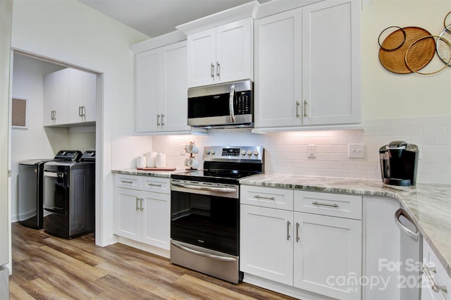 kitchen featuring light wood finished floors, appliances with stainless steel finishes, white cabinets, light stone countertops, and washer and dryer