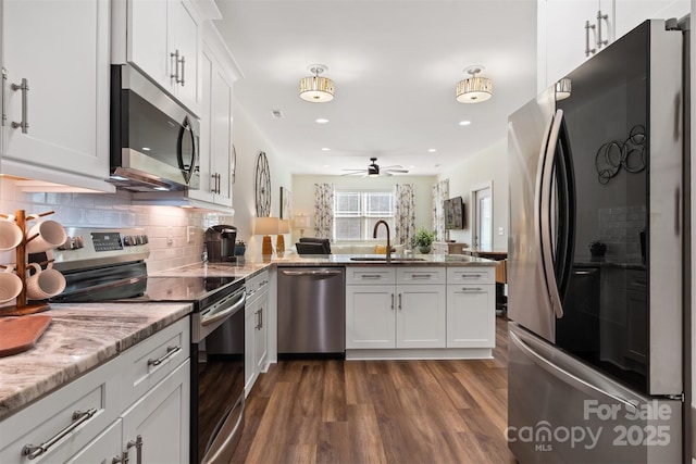 kitchen featuring a peninsula, light stone countertops, stainless steel appliances, white cabinetry, and a sink