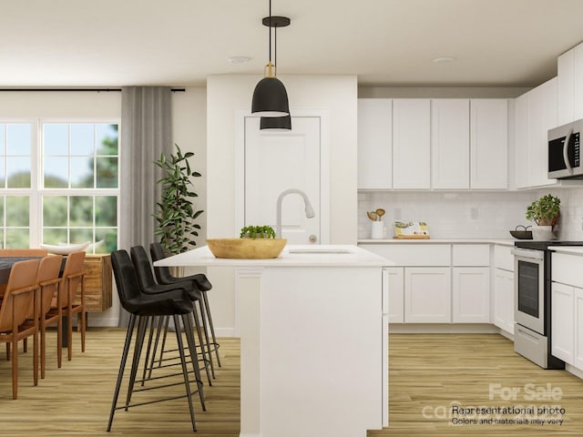 kitchen with hanging light fixtures, stainless steel appliances, an island with sink, backsplash, and white cabinetry