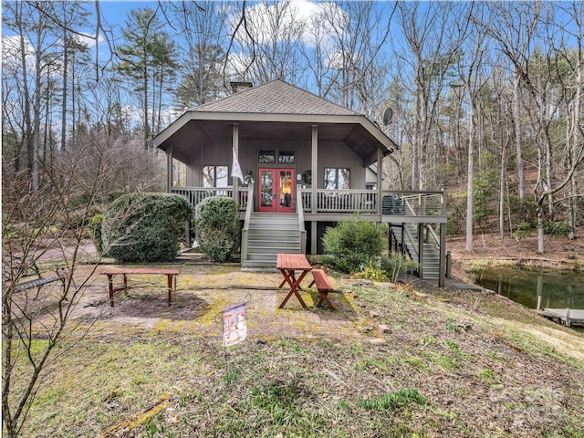 view of front of house featuring stairs, french doors, a chimney, and a shingled roof