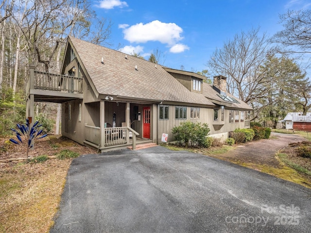 rustic home featuring driveway, a chimney, roof with shingles, covered porch, and board and batten siding