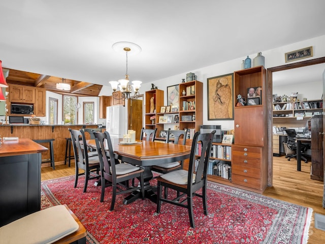 dining area featuring a chandelier, light wood finished floors, and beamed ceiling