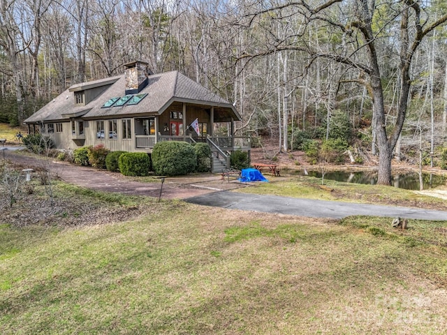 view of front of home featuring aphalt driveway, covered porch, a water view, stairs, and a front lawn