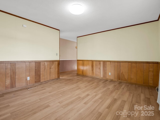 spare room with ornamental molding, light hardwood / wood-style floors, and wooden walls