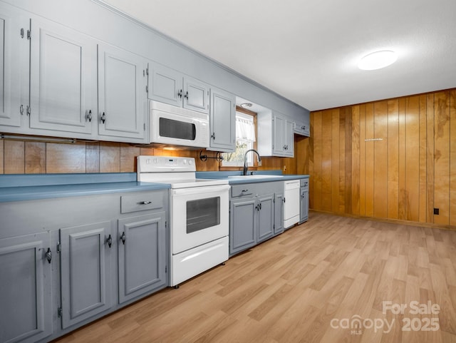 kitchen with sink, white appliances, wood walls, and light hardwood / wood-style floors