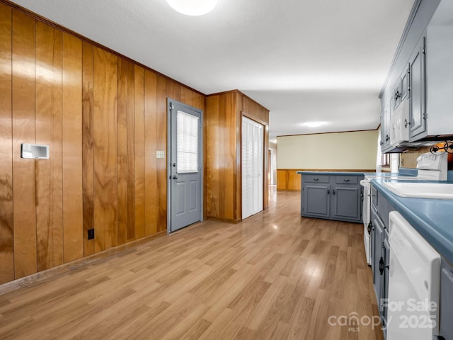 kitchen featuring sink, wood walls, light hardwood / wood-style floors, white dishwasher, and gray cabinets