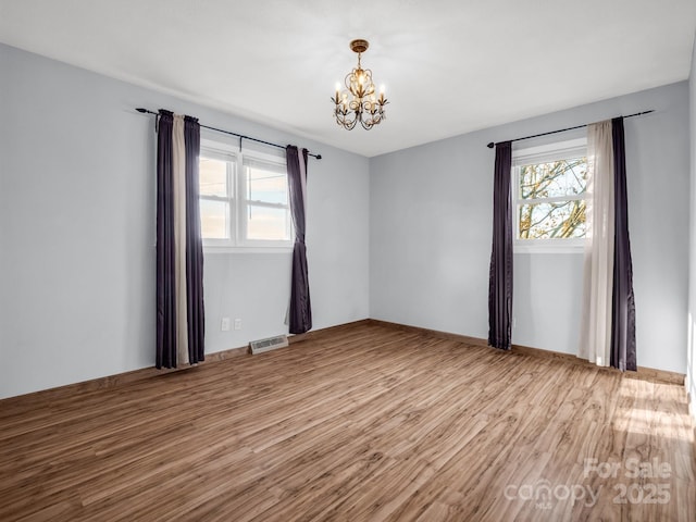 empty room featuring hardwood / wood-style flooring, a chandelier, and a wealth of natural light