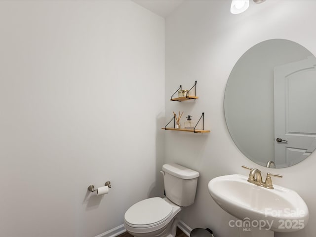 half bath featuring a sink, toilet, and baseboards