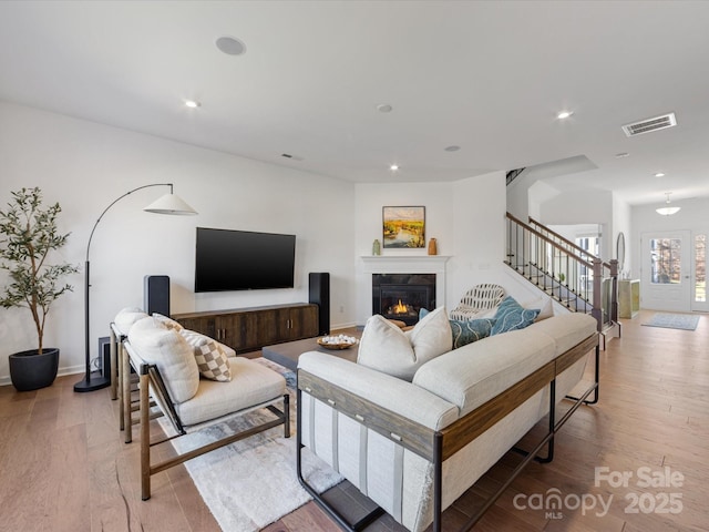 living area with a warm lit fireplace, visible vents, light wood-style flooring, stairway, and recessed lighting