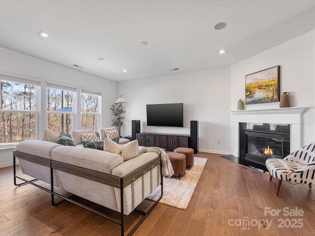 living room with baseboards, recessed lighting, a fireplace with flush hearth, and light wood-style floors