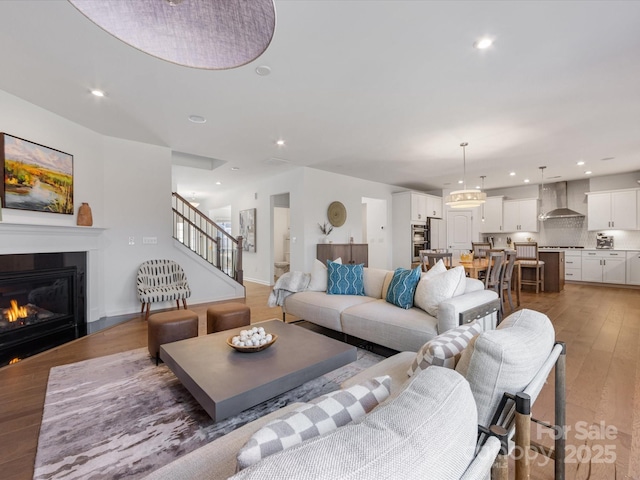 living area with dark wood-style floors, a glass covered fireplace, stairway, and recessed lighting