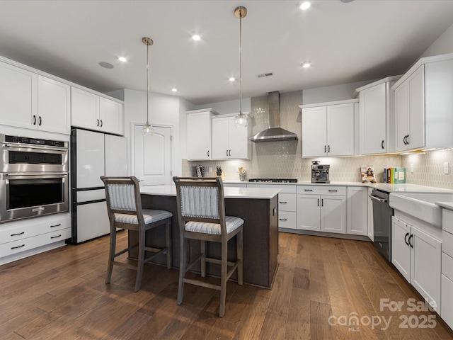 kitchen with pendant lighting, stainless steel appliances, light countertops, white cabinets, and wall chimney exhaust hood