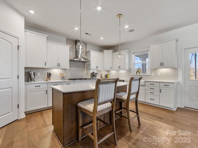 kitchen with light countertops, wall chimney exhaust hood, and white cabinetry