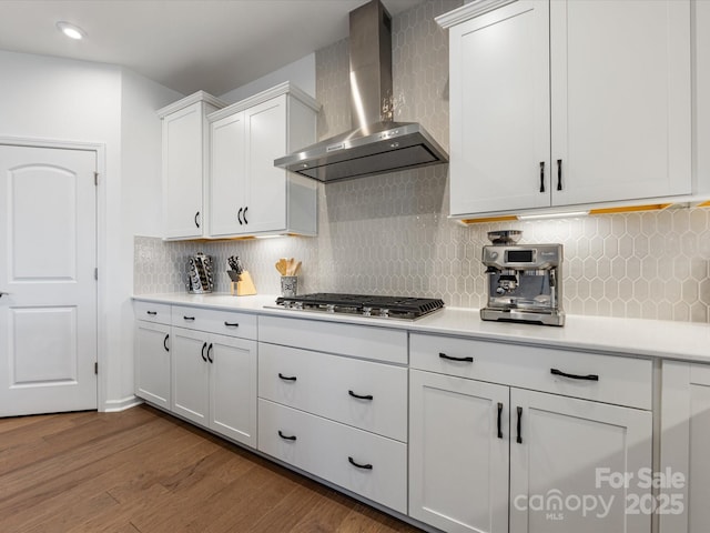 kitchen featuring dark wood-type flooring, white cabinets, light countertops, wall chimney exhaust hood, and stainless steel gas stovetop