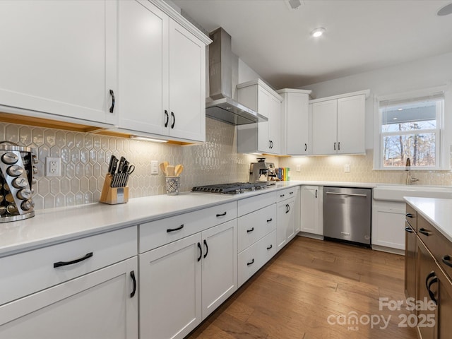 kitchen featuring wall chimney exhaust hood, appliances with stainless steel finishes, light countertops, and white cabinetry