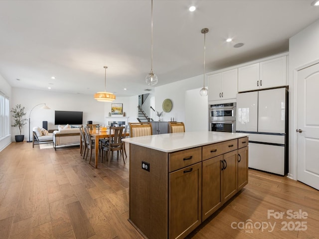 kitchen featuring a kitchen island, white cabinets, open floor plan, light countertops, and freestanding refrigerator