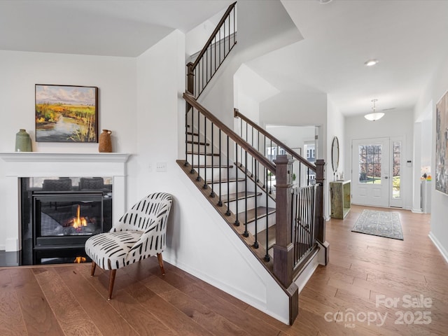 foyer entrance with recessed lighting, a glass covered fireplace, wood finished floors, baseboards, and stairs