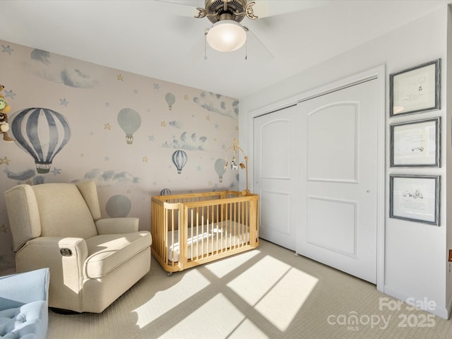 bedroom with a crib, wallpapered walls, a ceiling fan, carpet flooring, and a closet