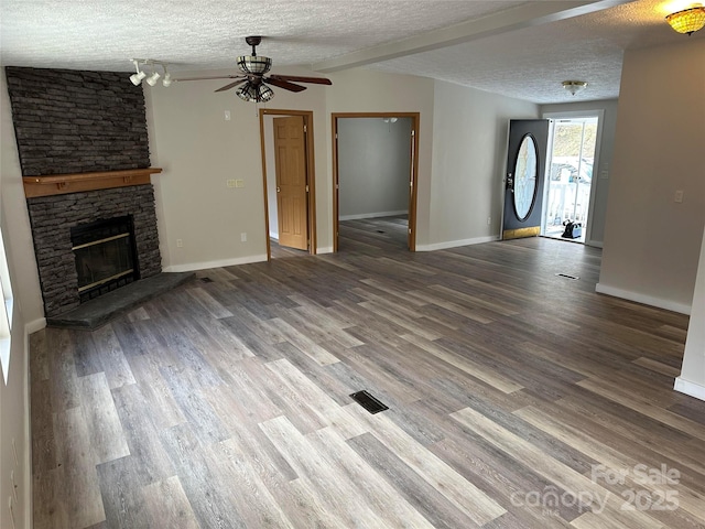 unfurnished living room with a stone fireplace, a textured ceiling, and wood finished floors