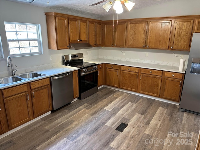 kitchen featuring under cabinet range hood, appliances with stainless steel finishes, brown cabinetry, and a sink