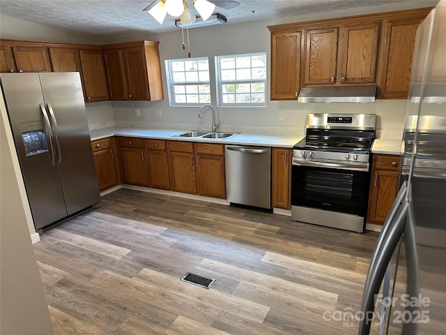 kitchen featuring stainless steel appliances, ventilation hood, a sink, and brown cabinets