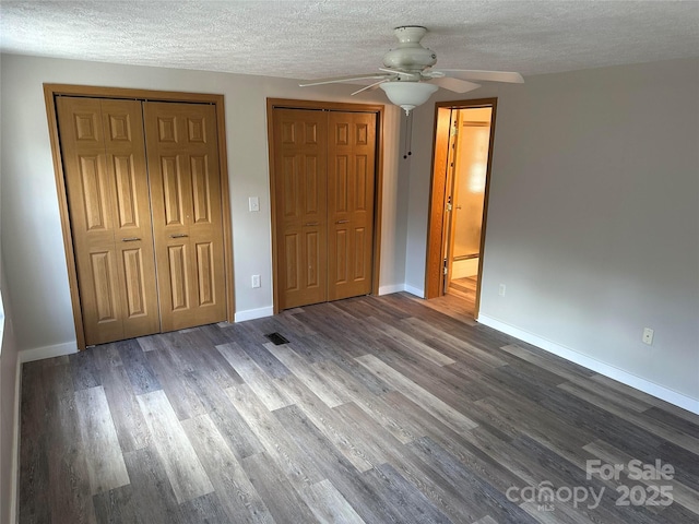 unfurnished bedroom featuring a textured ceiling, a baseboard heating unit, wood finished floors, baseboards, and two closets