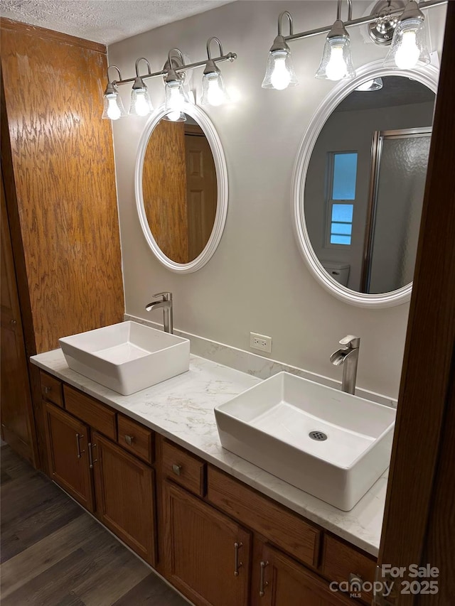 full bath with a textured ceiling, double vanity, wood finished floors, and a sink