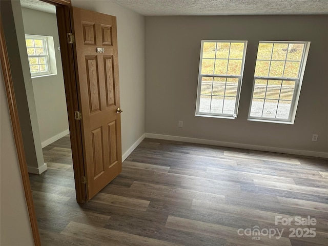 empty room with a textured ceiling, wood finished floors, and baseboards