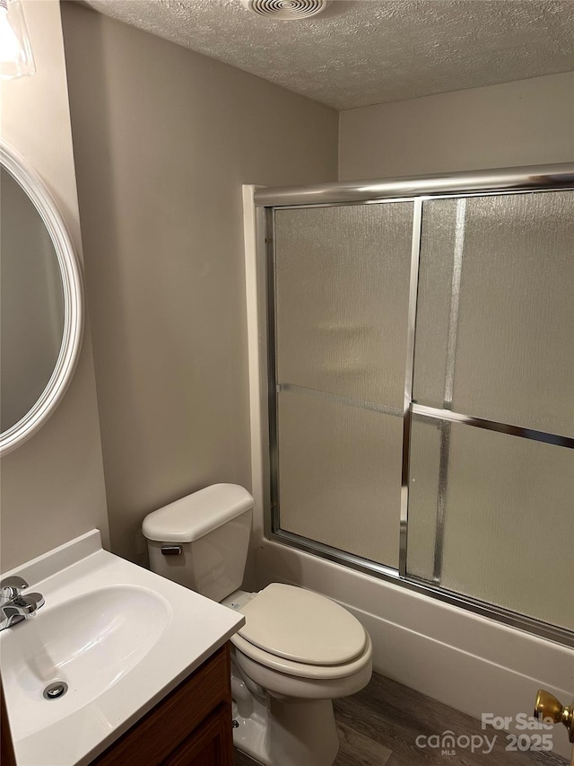 full bathroom with enclosed tub / shower combo, a textured ceiling, toilet, wood finished floors, and vanity