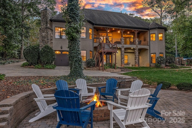 exterior space featuring concrete driveway, an outdoor fire pit, a patio area, a balcony, and stairs