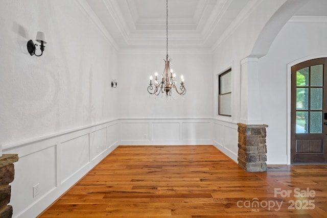 unfurnished dining area with light wood-type flooring, a tray ceiling, arched walkways, and a notable chandelier
