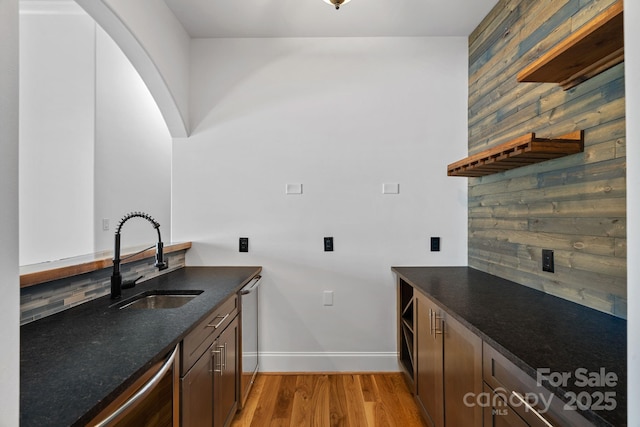 kitchen with wood walls, a sink, light wood-type flooring, dishwasher, and baseboards