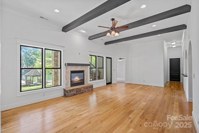 unfurnished living room with beam ceiling, baseboards, visible vents, a ceiling fan, and a stone fireplace