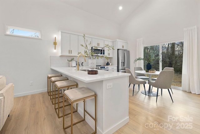 kitchen featuring stainless steel appliances, white cabinets, a breakfast bar, light wood-type flooring, and kitchen peninsula