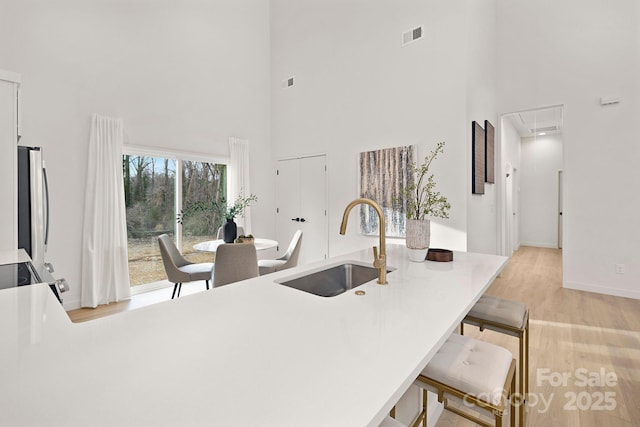 kitchen featuring light wood-type flooring, kitchen peninsula, stainless steel fridge, sink, and a breakfast bar area